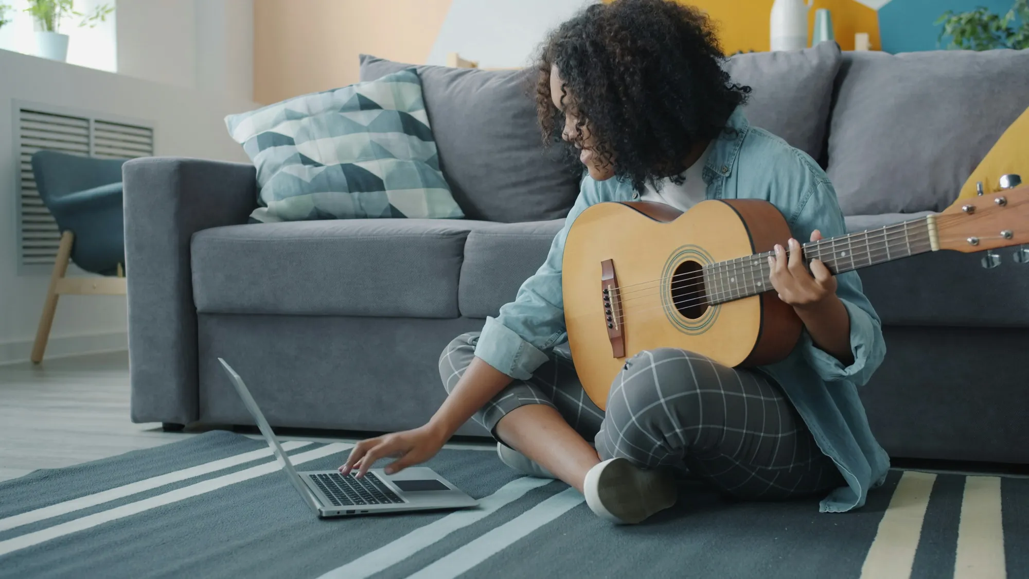 Una ragazza con la chitarra seduta sul tappeto che scrive al portatile