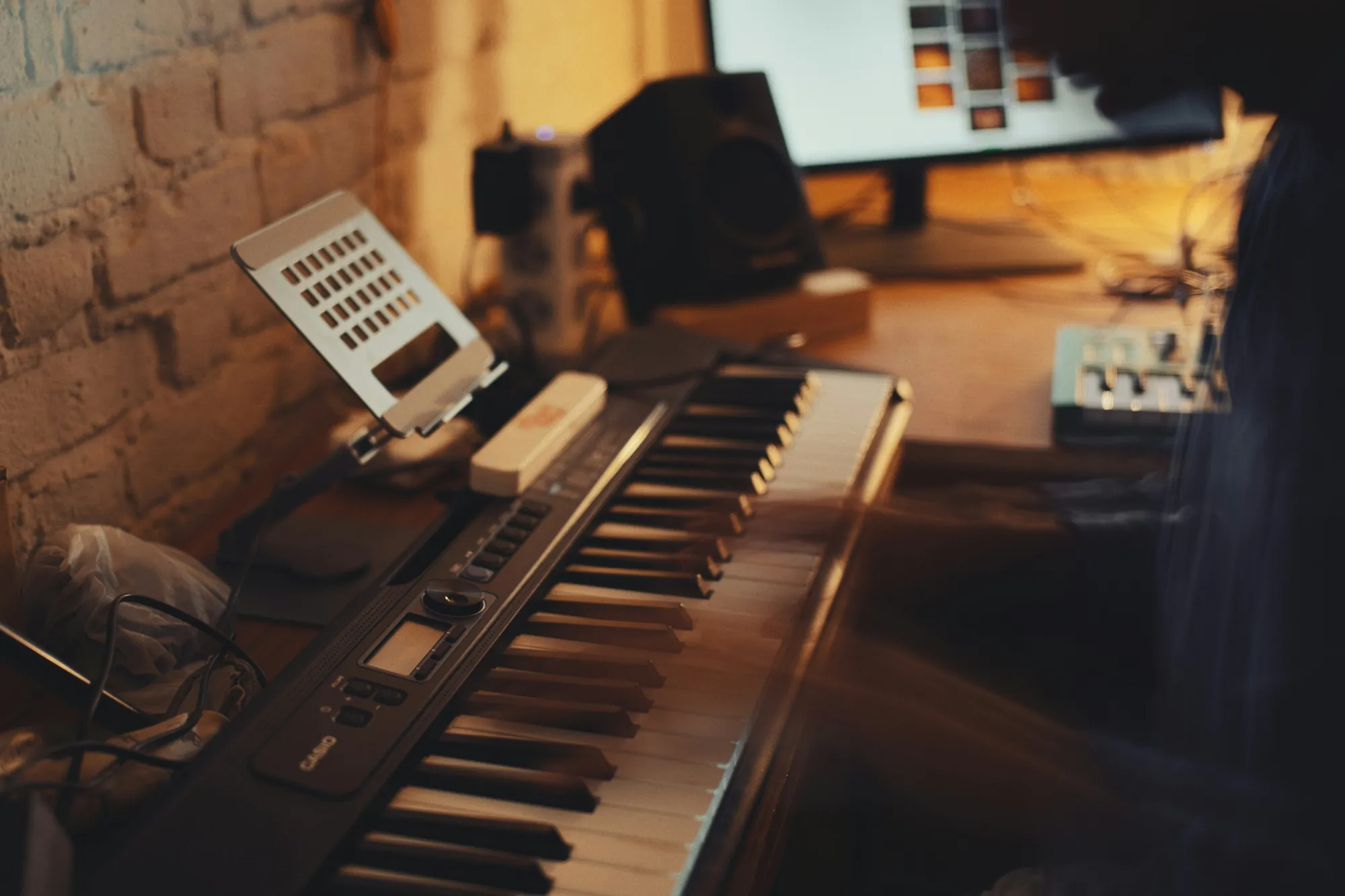 Una persona che suona una tastiera digitale nel suo studio di casa, con il computer accanto